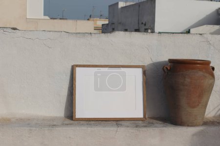 Photo for Blank horizontal wooden frame picture mock up. Vintage olive clay storage pot, vase. White old textured white wall in sunlight. Front view, no people, summer display background for art, posters. - Royalty Free Image