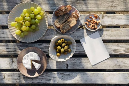 Summer food, picnic. Brie cheese, grapes fruit, olives and cashew nuts. Bread, baguette. Vintage white wooden table top view. Greeting card, invitation mockup. Free copy space. Flatlay. Delicious