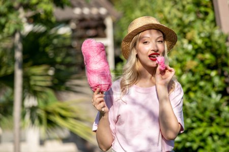 Photo for Cute girl lovely pretty young blonde girl in hat in the summer at the park with cotton candy - Royalty Free Image