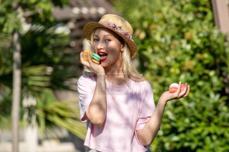 Photo for Cute girl young lovely pretty blonde girl in hat in the summer at the park eating macaroons - Royalty Free Image
