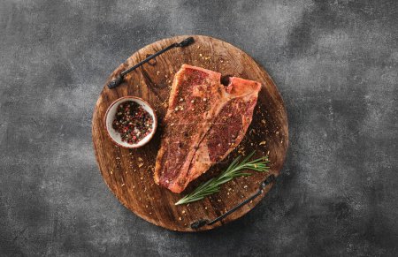 Téléchargez les photos : Viande fraîche crue T-bone steak, assaisonnement sur planche à découper sur fond gris - en image libre de droit