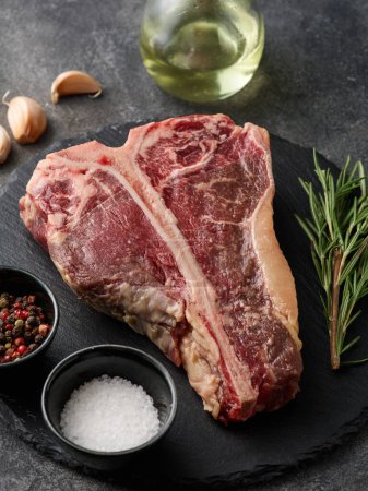 Photo for T-bone or porterhouse raw steak of beef cut from the short loin. Raw fresh beef T-bone steak with rosemary, salt and pepper - Royalty Free Image