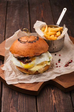 Téléchargez les photos : Une image en gros plan d'un cheeseburger au bacon gourmet juteux avec des frites croustillantes sur une table en bois. - en image libre de droit