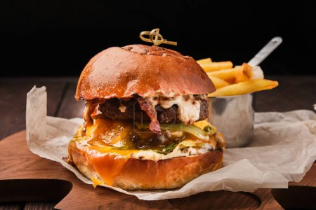 Foto de Una imagen de cerca de una jugosa hamburguesa gourmet de tocino con papas fritas crujientes en una mesa de madera. - Imagen libre de derechos