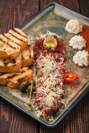 Photo for A delicious serving of steak tartare garnished with egg yolk and cheese, accompanied by grilled bread slices. The dish is presented on a rustic ceramic plate, capturing the essence of fine dining. - Royalty Free Image