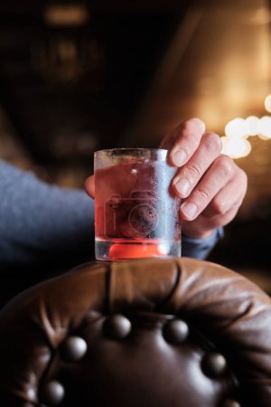 Une image en gros plan capturant un moment de quelqu'un tenant un verre de cocktail cerise, garni d'une cerise, dans un bar bien éclairé.