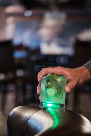 Téléchargez les photos : Concombre rafraîchissant et cocktail à la menthe dans un verre carré. La boisson est illuminée d'en bas, soulignant sa couleur verte vibrante et les bulles. Des tranches de concombre frais et des brins de menthe sont visibles à l'intérieur du verre. - en image libre de droit