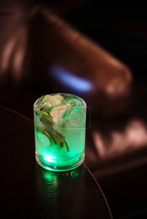 Ein bezauberndes Bild eines leuchtend grünen Cocktails, serviert mit Eis und Garnitur, schafft ein einladendes Ambiente in einem dunklen, luxuriösen Ambiente