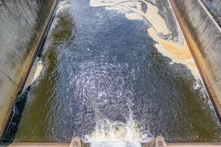 Téléchargez les photos : Eau qui coule de la porte du barrage de Staumauer Bitburger à Prum rive, pollution par une tache brune à la surface de l'eau, réservoir de Stausee Bitburg, journée ensoleillée de printemps en Allemagne - en image libre de droit