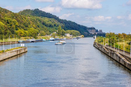 Photo for Lanaye canal at lock with anchored cargo ships, one sailing, mountains part of nature reserve in Belgian part of Sint-Pietersberg with lush green trees, sunny summer day in Ternaaien, Belgium - Royalty Free Image