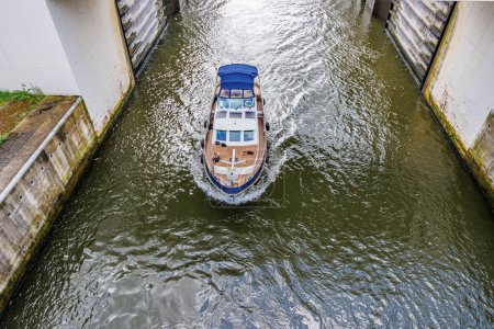 Téléchargez les photos : Angle supérieur d'un petit bateau quittant l'écluse de Lanaye avec la porte d'inondation ouverte vers le canal Albert, immenses murs à faible niveau d'eau, journée d'été nuageuse à Ternaaien, Belgique - en image libre de droit