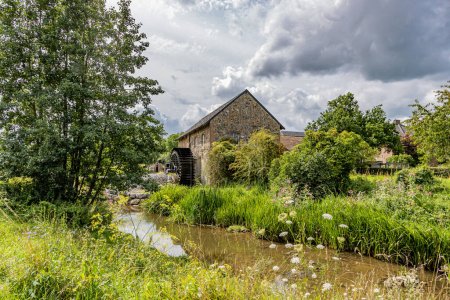 Photo for River landscape with river Geul and old Eper watermill or Wingbergermolen in background, surrounded by vegetation and wild trees, cloudy sky day at Terpoorterweg, Epen, South Limburg, Netherlands - Royalty Free Image