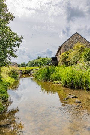Photo for Low angle perspective of Geul river, old Eper watermill or Wingbergermolen against gray sky in background, wild vegetation and lusch trees, cloudy day in Terpoorten, Epen, South Limburg, Netherlands - Royalty Free Image