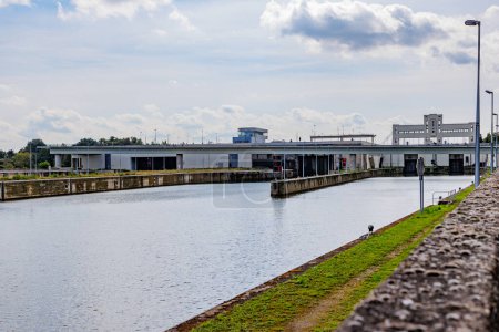 Photo for Canal towards Lanaye lock complex with closed floodgates, Albert canal, construction walls, vehicular bridge in background against misty sky, sunny summer day in Ternaaien, Belgium - Royalty Free Image