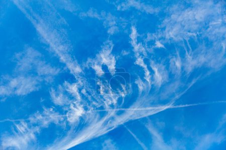 Cirrus clouds and water vapor trails left by airplanes against clear blue sky in background in sunny day, form of thin filaments