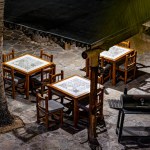 Aerial view of square tables and wooden chairs on terrace of small restaurant, illuminated by light of lamps, stone floor, metal grill, quiet night in Baja California Sur, Mexico