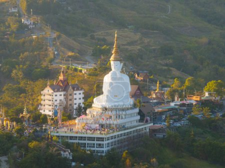 Luftaufnahme einer majestätischen weißen Buddha-Statue auf einem Hügel mit einem malerischen Sonnenuntergang, mit Blick auf eine geschäftige Stadt unten.