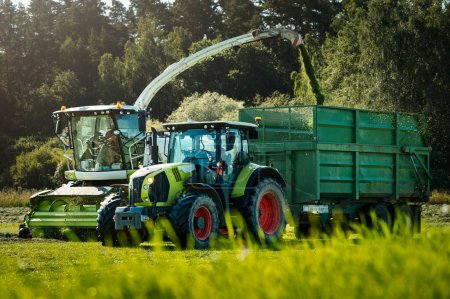 Téléchargez les photos : Champ agricole avec tracteurs ramassant de l'herbe pour l'ensilage, fin d'été - en image libre de droit