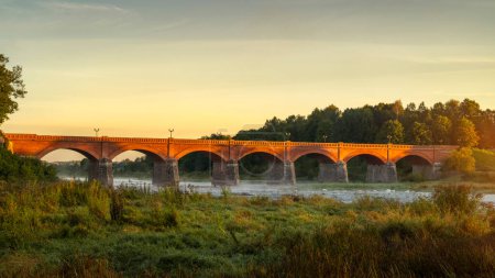 Téléchargez les photos : Pont en pierre sur la rivière Venta à côté de la plus large chute d'eau en Europe-Ventas Rumba à Kuldiga, Lettonie, au lever du soleil en automne - en image libre de droit