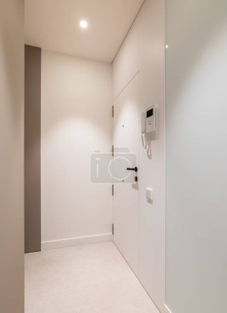Photo for Vertical view of entrance hall area in modern refurbished apartment. White walls and door with intercom system - Royalty Free Image