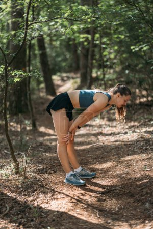 Young woman in sportswear tired and resting in the forest after working out. Trail running and active life concept