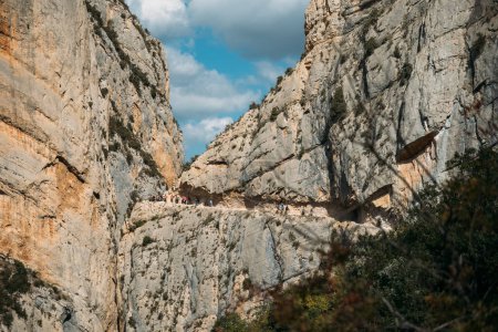 Spectacular cliff with a walkway inside the rock with people doing hiking trips. Congost de Mont Rebei, Catalonia, Spain
