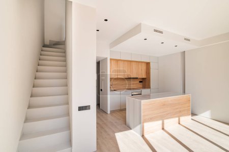 Téléchargez les photos : Intérieur vide de duplex rénové avec escalier et cuisine moderne avec îlot et meubles en bois. - en image libre de droit