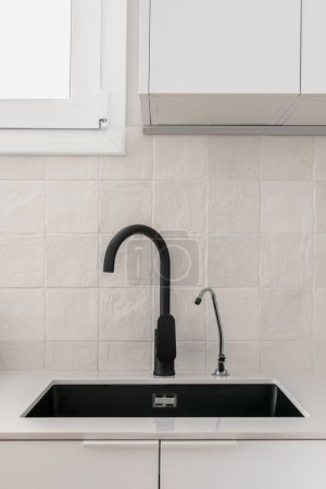 Detail eines einfachen schwarzen Waschbeckens mit Wasserhahn und kleinem Filterhahn für Trinkwasser
