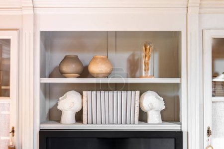 Head shaped bookends with books and clay pot on a shelf indoors. Interior design