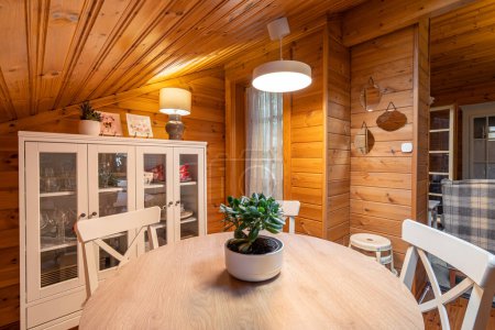 Dining room in a cozy wooden house. Rural style room with table, chairs, cupboard and decorative elements