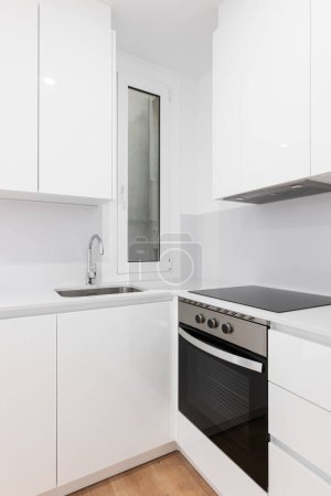 Vertikale Aufnahme einer modernen weißen Küche mit Schränken, schwarzem Herd, Backofen und Dunstabzugshaube.