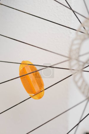 La photo montre une perspective abstraite et minimaliste d'un réflecteur bicyclette jaune vif monté entre les rayons noirs d'une roue