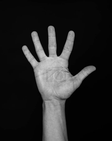 A human hand raised with fingers spread against a stark black background.