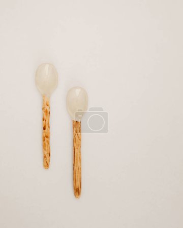 Dieses Bild zeigt zwei handgefertigte Keramiklöffel mit rustikalen Holzgriffen, die auf einem weißen Hintergrund ausgelegt sind.