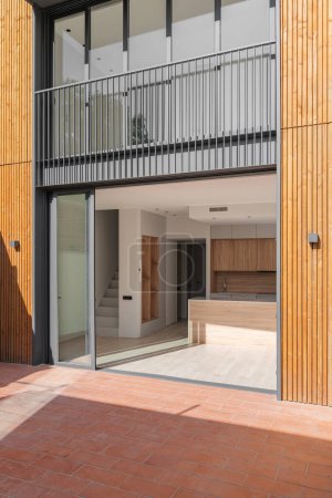 Glastüren in schwarzem Metallrahmen öffnen sich zum Haus mit geräumiger Küche mit hellen Holzmöbeln und Treppe in den zweiten Stock. Türen verbinden die Rückseite des Hauses und den Innenhof