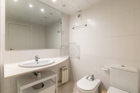 Einfaches weißes Badezimmer mit großem Spiegel, klassischem Waschbecken, Bidet und Toilette