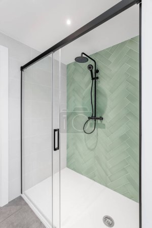 Téléchargez les photos : Salle de bain moderne avec carrelage vert clair et blanc, tête de pluie, douche à main et porte en verre - en image libre de droit