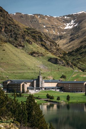 Beautiful valley of Vall de Nuria is picturesque breathtaking place in Spain. Temple of Nuria on shore of lake at foot of mountain is flooded with bright sunlight on clear cloudless day