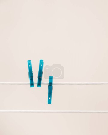Zwei blaue Wäscheklammern hängen an einer Wäscheleine vor weißem Hintergrund.