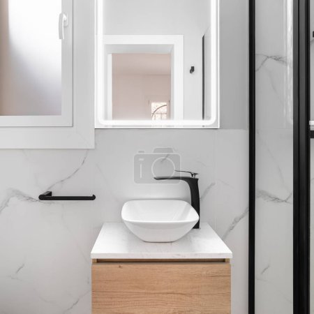 Helles Badezimmer verfügt über einen eleganten und minimalistischen Stil, mit einem strahlend weißen Waschbecken vor einem atemberaubenden, schwarz umrahmten Spiegel, der einen modernen und raffinierten Look schafft