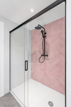 Téléchargez les photos : Salle de bain moderne avec carrelage rose et blanc, tête de pluie, douche à main et porte en verre - en image libre de droit
