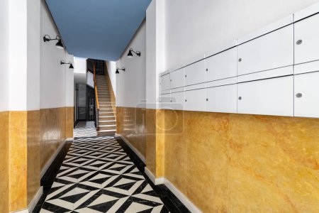 Foto de Vestíbulo en la entrada de la casa con pasillo largo, escaleras al segundo piso, suelo de mosaico de mármol blanco y negro, paredes de color amarillo brillante, lámparas en pantallas de metal negro y buzones - Imagen libre de derechos