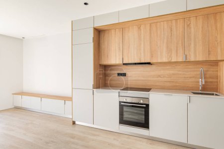 Cuisine minimale contemporaine et salon avec balcon dans un appartement rénové vide. Meubles en bois et appareils modernes.