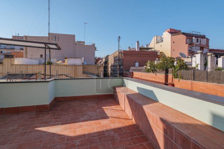 Big sunny terrace on the roof of modern building lined with red brick tiles overlooking the neighboring houses. Summer playground for leisure activities, party and meetings with friends