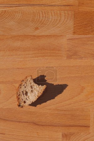 Eine einzige Scheibe Brot wirft einen Schatten auf eine Holzoberfläche