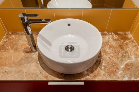 Une salle de bain ronde évier blanc avec un robinet et un miroir.