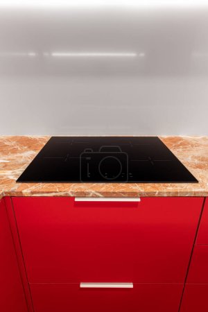 Red kitchen with black stove. Rectangle-shaped hardwood cabinets.