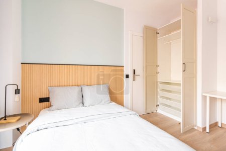 Photo for Hotel room with large double bed, beautiful linens. There is wood paneling on wall at headboard. Large wardrobe for clothes and shoes. The door is electronically locked with digital code - Royalty Free Image