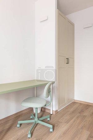 Ein Teil des Wohnzimmers mit weißen Wänden, Einbauschrank, Parkettboden in Holzoptik. An der Wand steht ein Arbeitstisch mit einer mintfarbenen Platte und einem mintfarbenen Lederstuhl