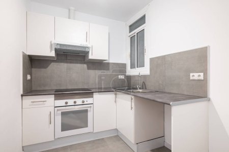 Light compact kitchen with stove, extractor hood and sink and window. Concept of kitchen in a small apartment. Modern minimalist design in new buildings.